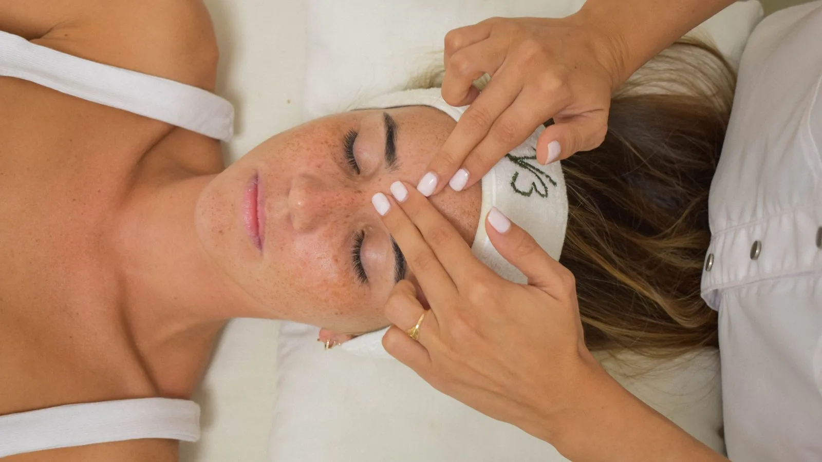 Therapeutin behandelt mit den Fingerspitzen das Gesicht einer liegenden Patientin