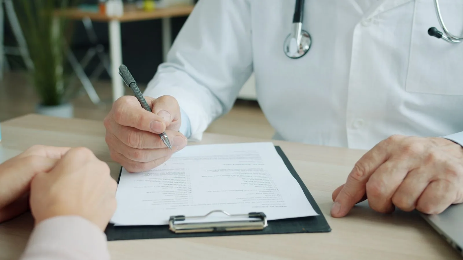 Arzt füllt mit einem Patienten ein Formular auf dem Klemmbrett aus